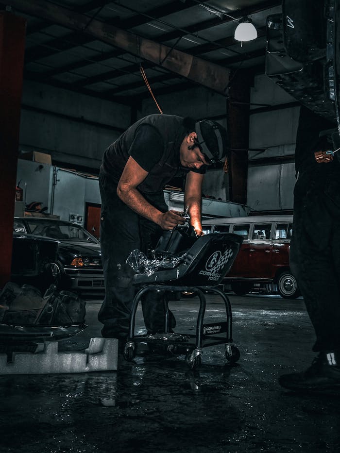 expertise-01 A mechanic focused on a car part repair in a dimly lit auto body shop.