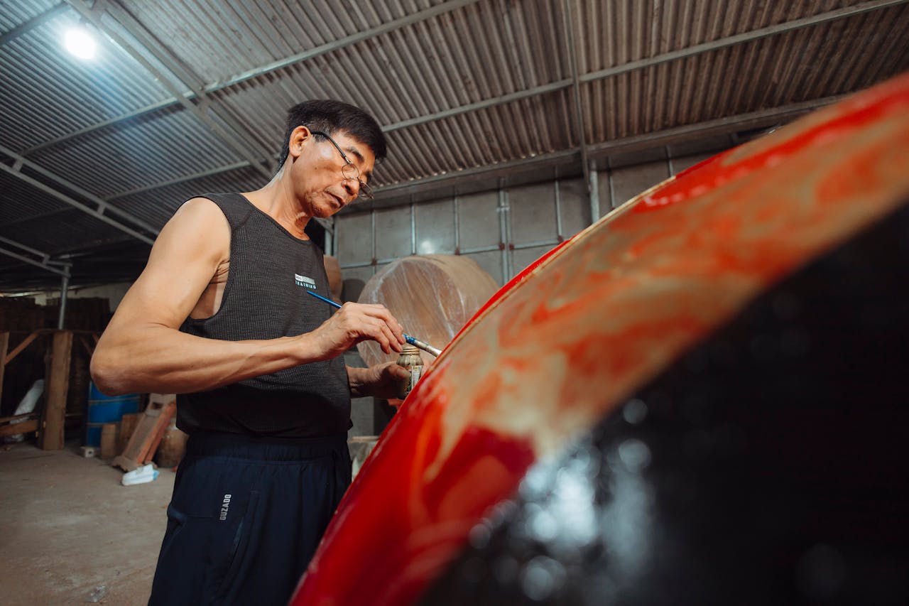 An adult male meticulously applies paint to a car in a garage setting with focused attention.